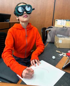 girl in a red sweatshirt wearing VR goggles and sketching on a paper
