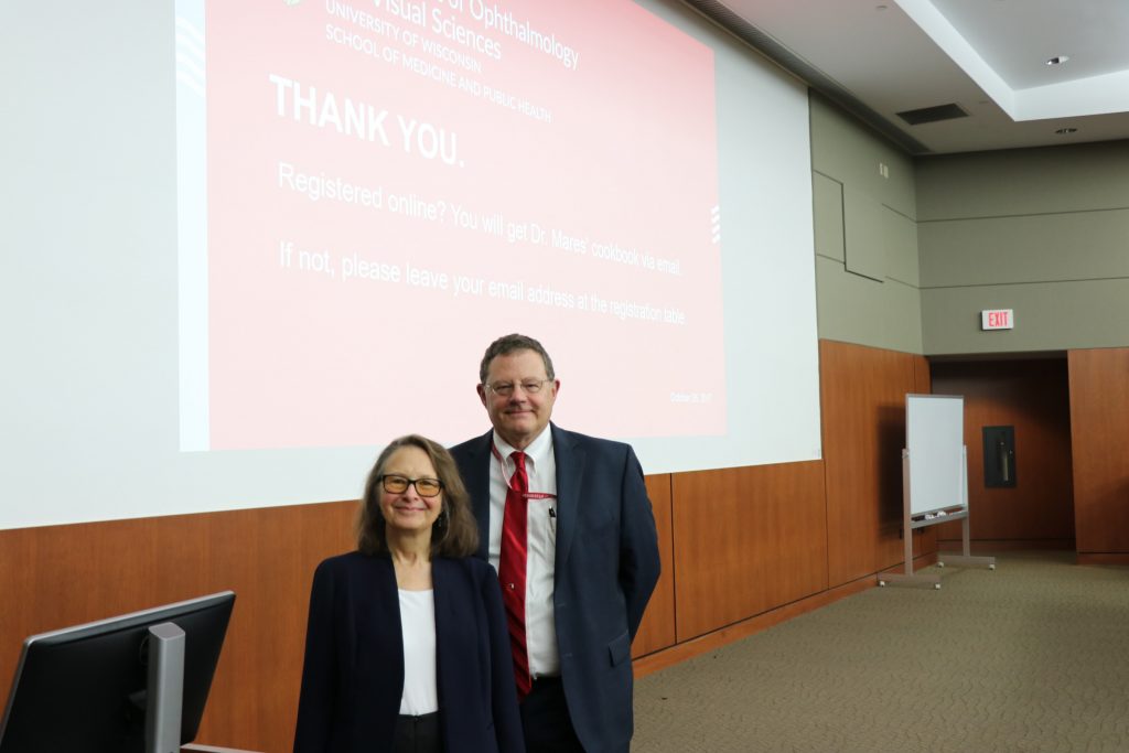 a woman and man stand in front of a large presentation screen