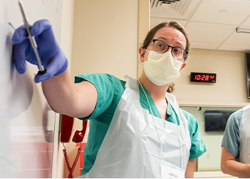 Clinician in surgical scrubs demonstrates processes on a whiteboard