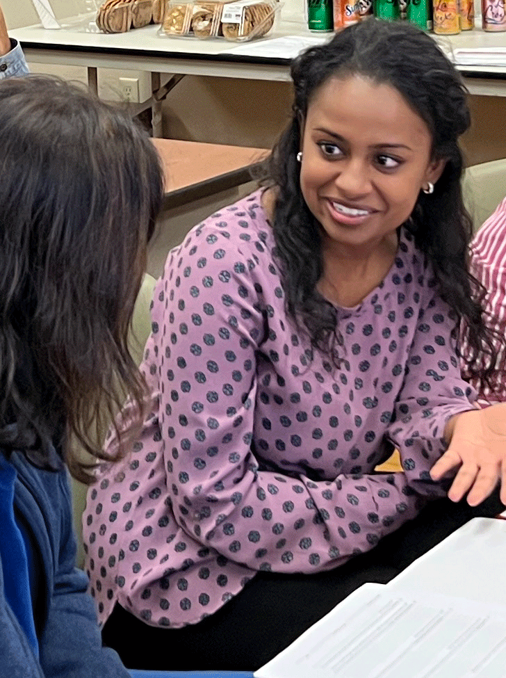 woman with dark hair wearing a purple shirt smiles at a woman in a blue sweatshirt