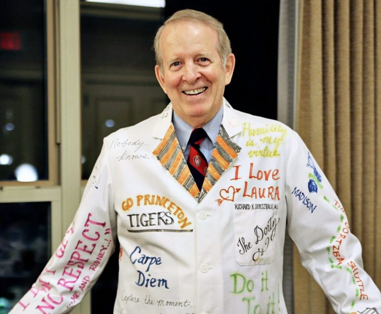 older gentleman wearing a white doctor's coat with signatures on it