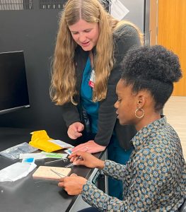 a woman practices sutures under the guidance of a female instructor