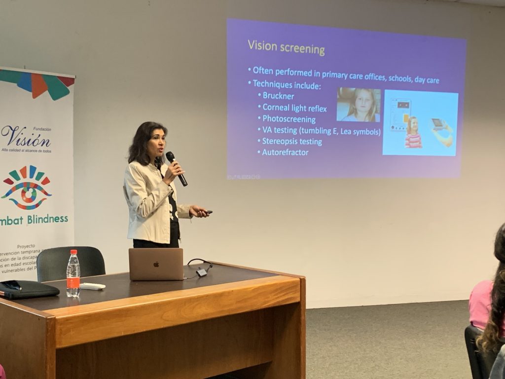 A woman in a cream colored jacket delivers a lecture on vision screening