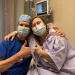 a man in blue surgical scrubs and a woman in a purple hospital gown give 'thumbs up'