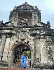 two women in blue scrubs stand underneath a historic arch