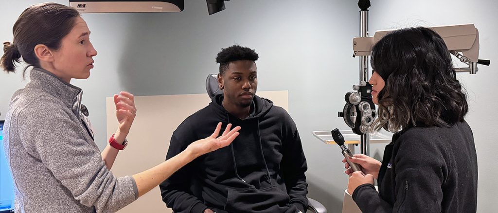 a faculty member talks to two students in an ophthalmology office