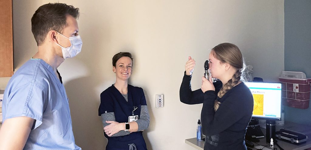 a woman looks though an eye exam tool with two people look on