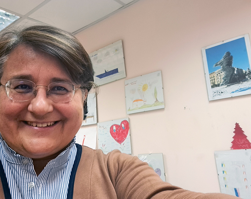 woman takes a selfie in front of a wall filled with children's drawings