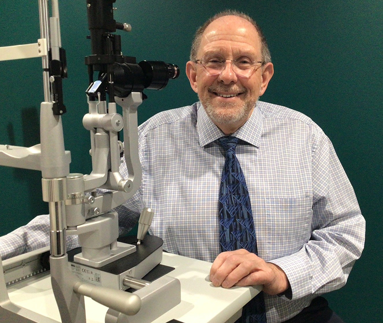 man in a blue checkered shirt and blue tie behind a slit lamp